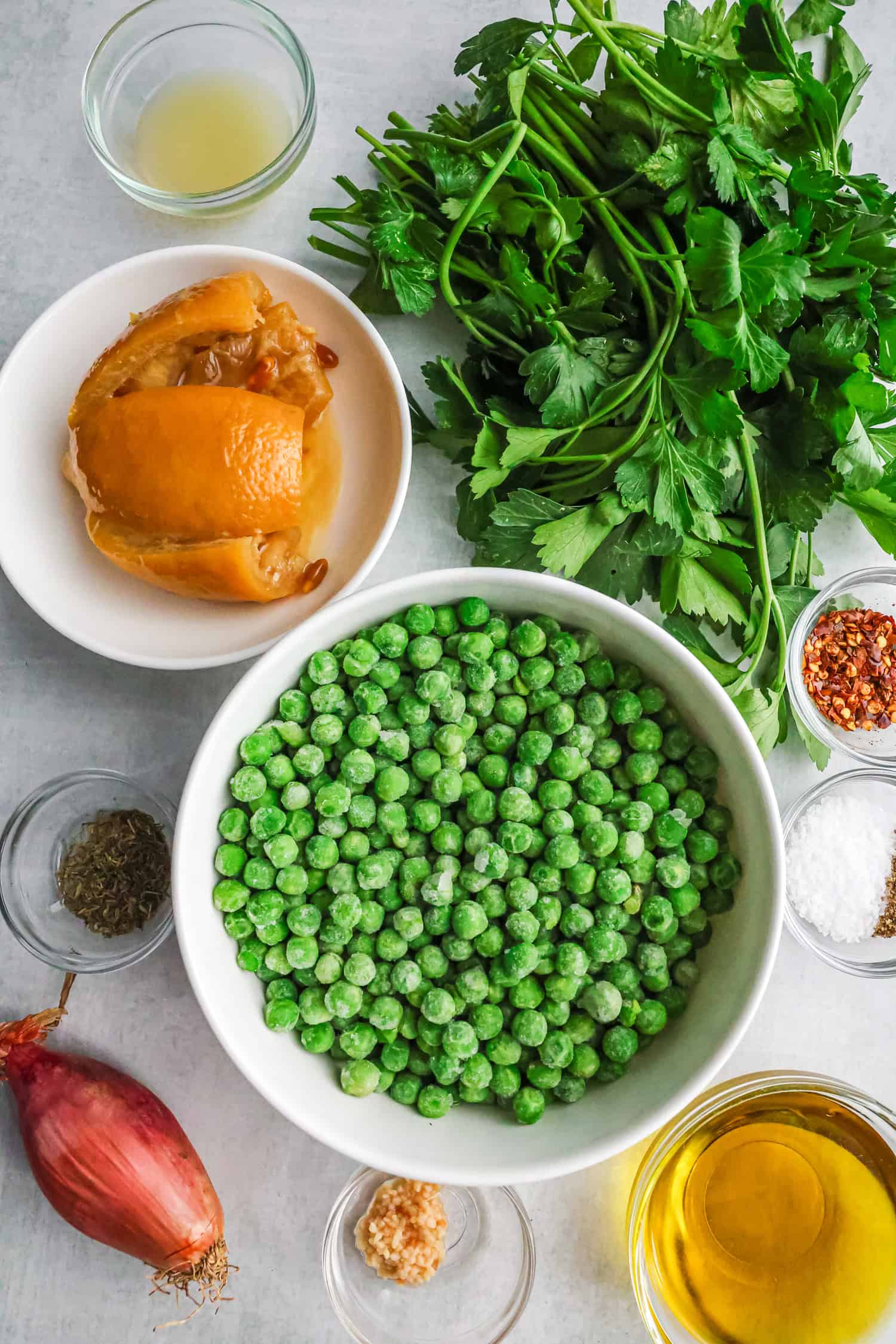 A top-down view of ingredients for a pea spread recipe, including a bowl of green peas, fresh parsley, preserved lemon, and small bowls of spices.