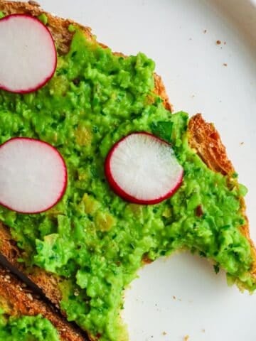 A piece of toasted sourdough bread topped with a thick layer of bright green mashed pea spread and sliced red radishes.