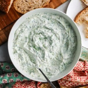 A white bowl of creamy Greek tzatziki sauce mixed with fresh green dill and cucumber.