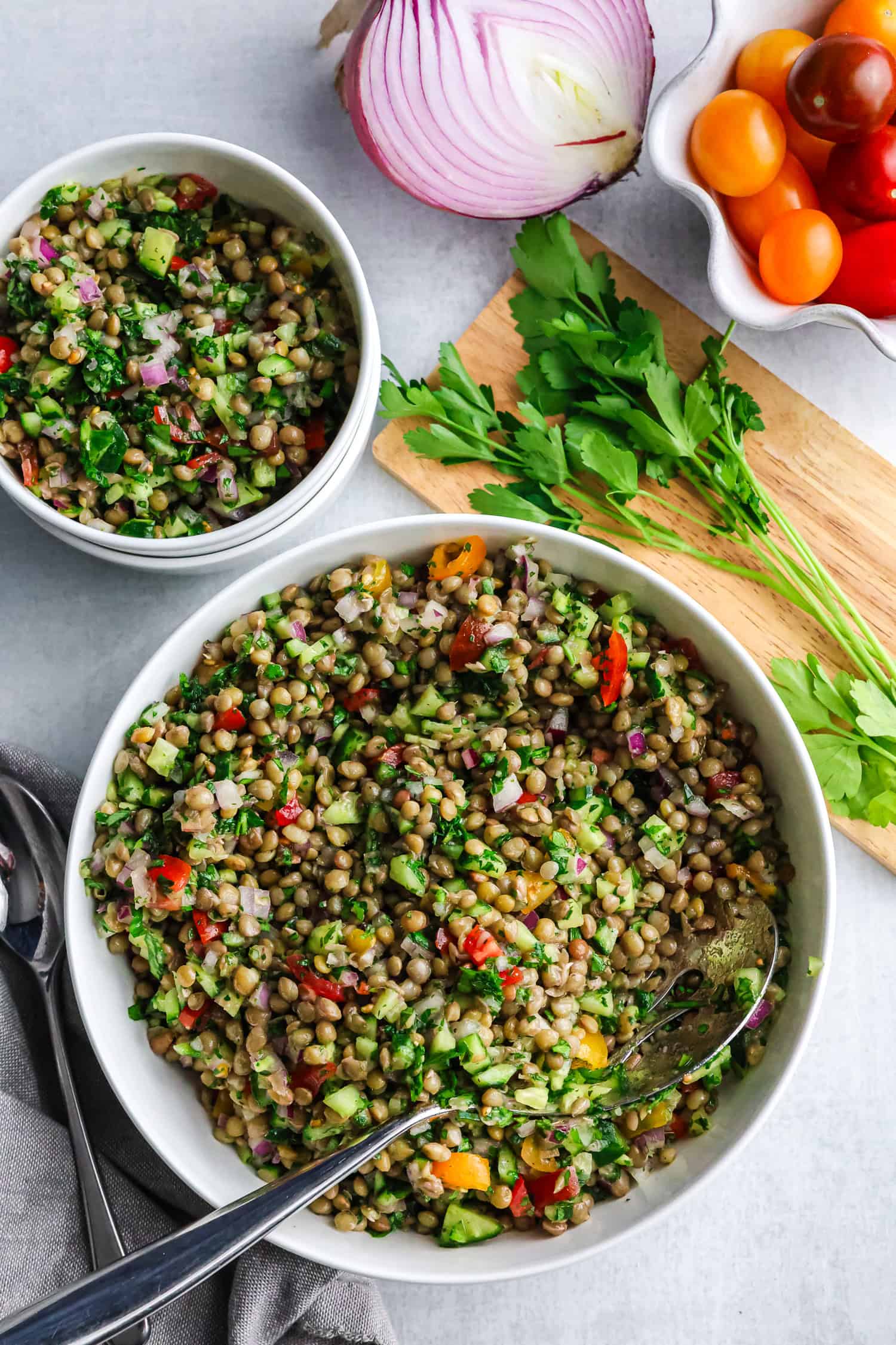 A large white bowl and a smaller bowl are filled with healthy lentil tabbouleh salad next to fresh vegetables.