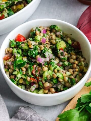 A white bowl filled with lentil tabbouleh salad featuring green lentils, diced cucumbers, tomatoes, red onions, and fresh parsley.