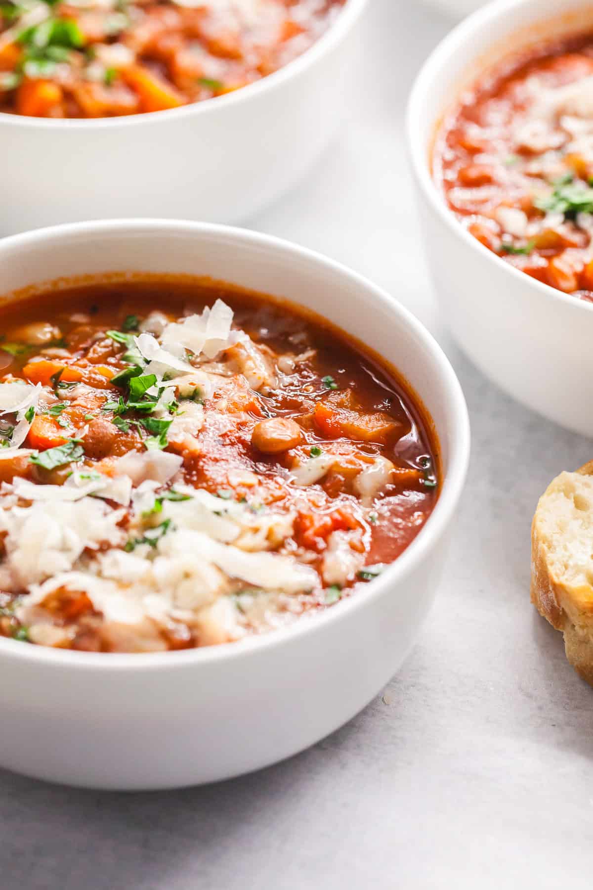 A bowl of lentil soup served with shaved Parmesan and chopped parsley and a slice of bread on the side