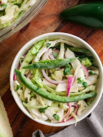 Jalapeño coleslaw served in a small bowl next to some cabbage and jalapeños