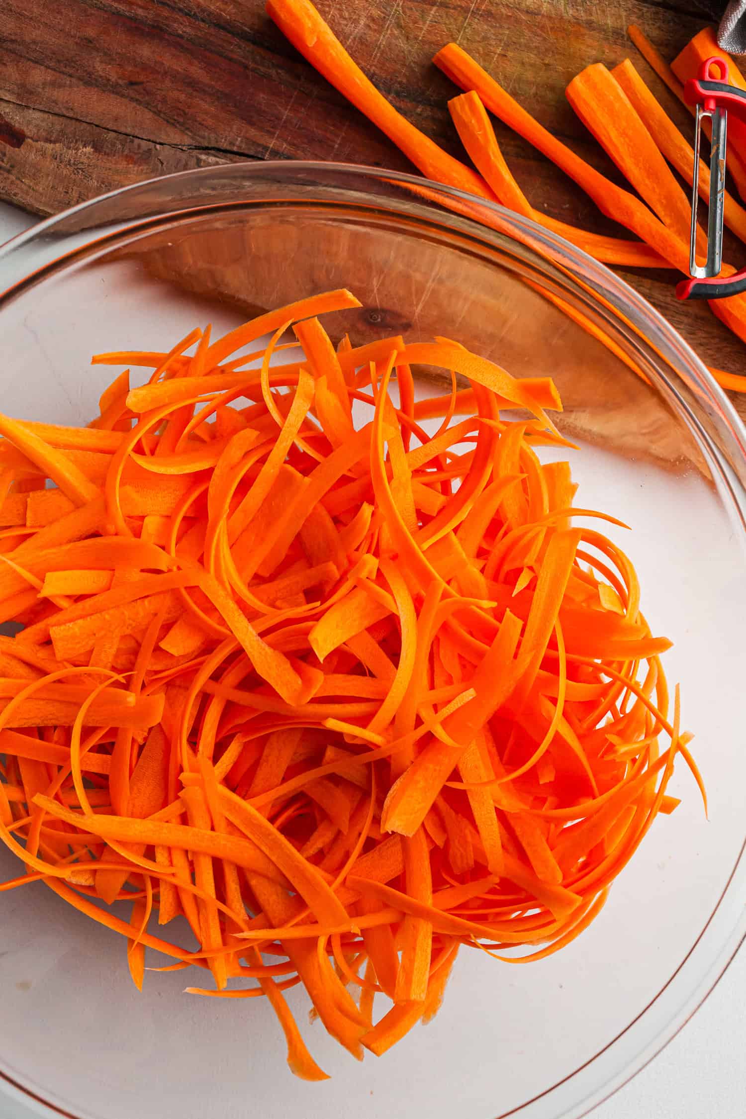 Glass bowl filled with thin carrot strips, placed on a wooden table.
