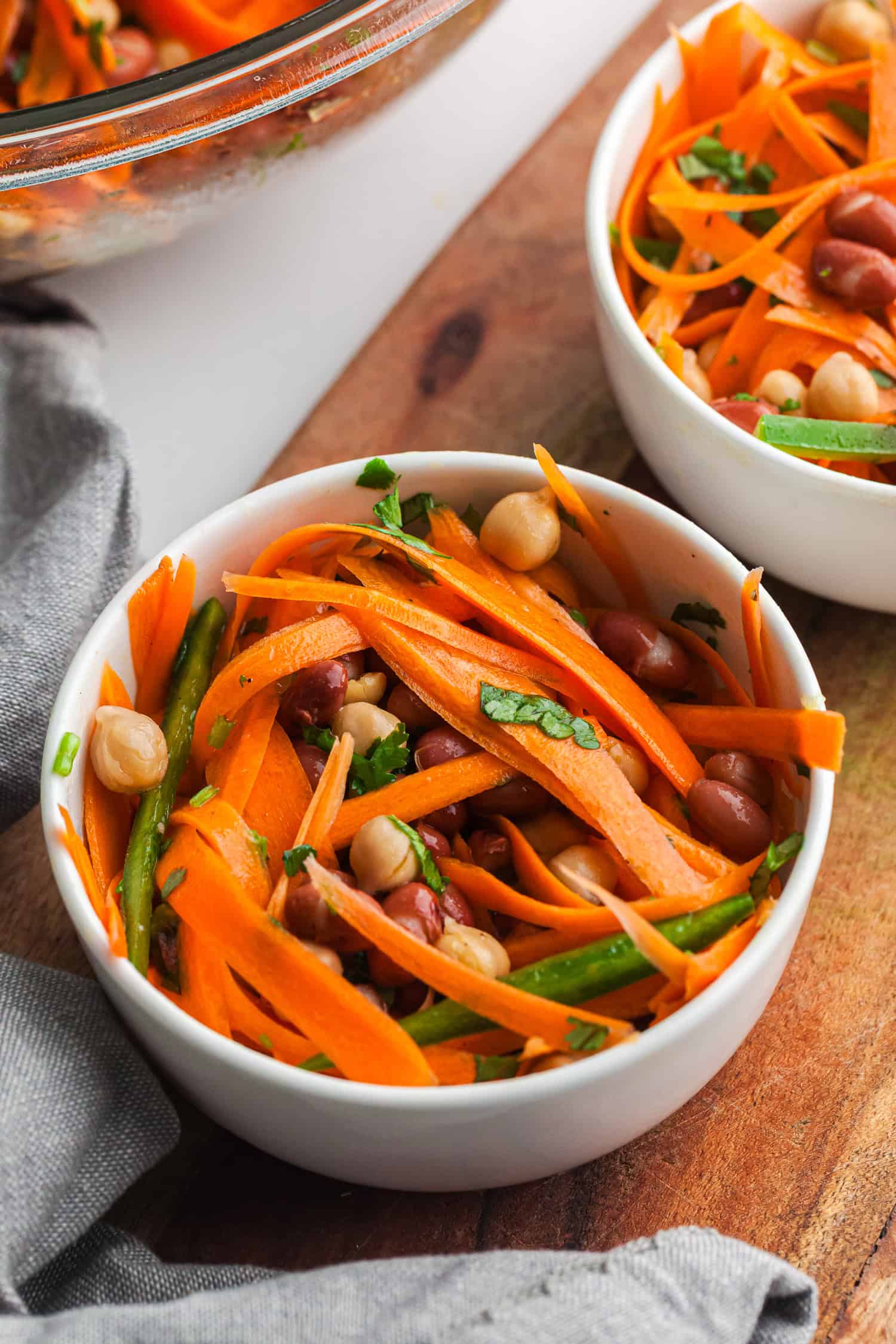 Fresh salad in a white bowl with ribboned carrots, chickpeas, green beans, kidney beans, and black-eyed peas.