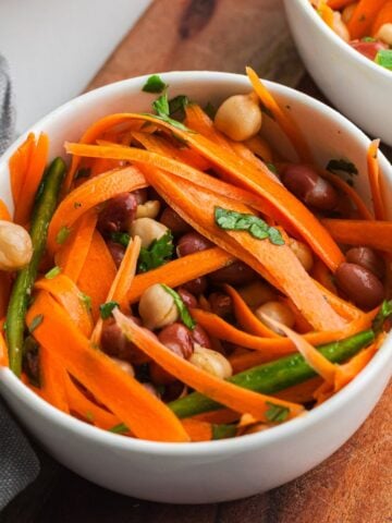 Bowl of colorful salad with ribboned carrots, chickpeas, kidney beans, green beans, and sliced jalapeños. Tossed in a light dressing and topped with pistachios.