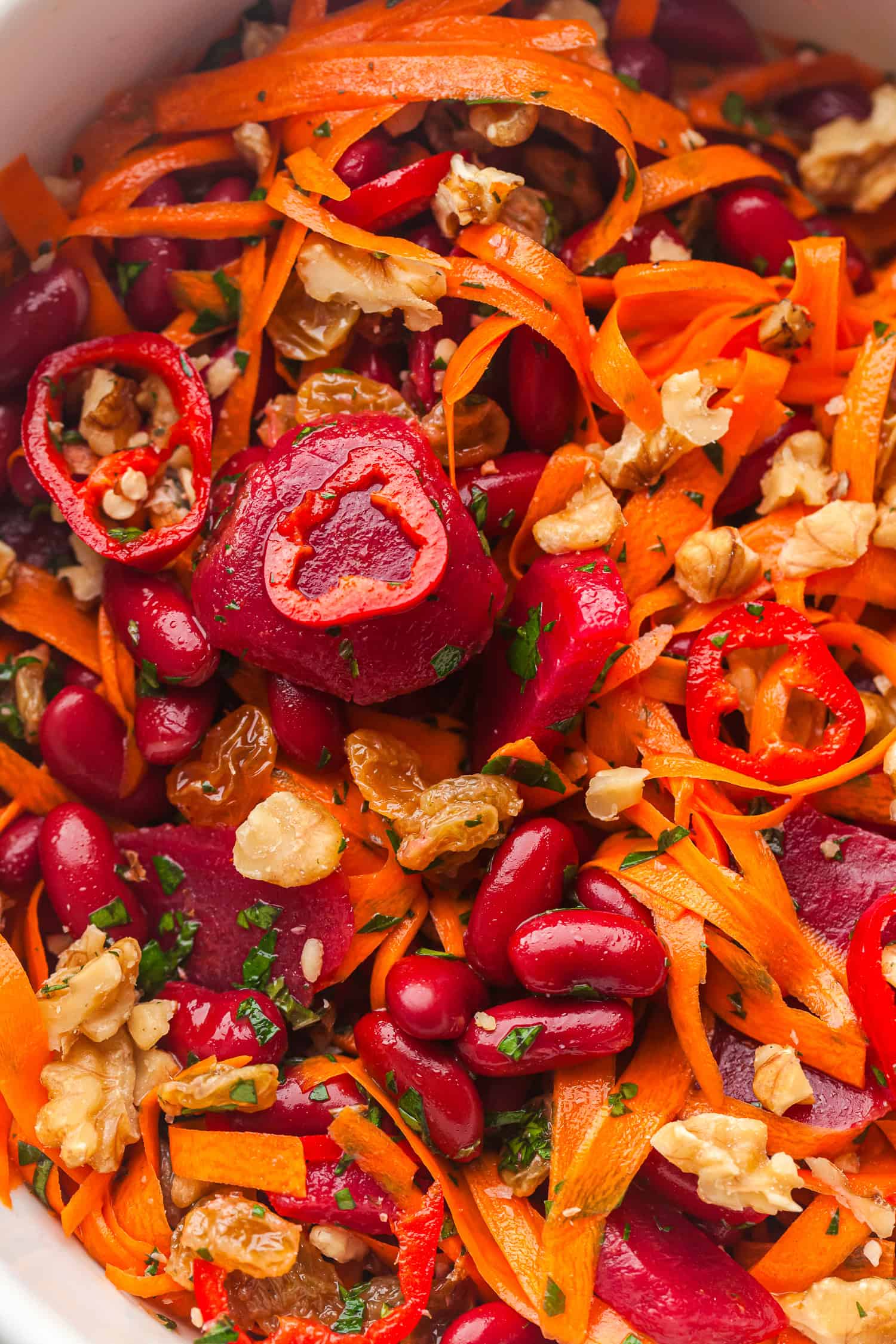 Fresh carrot and beet salad with beans, chili, walnuts, raisins, and herbs in a white bowl – healthy and colorful vegan food.