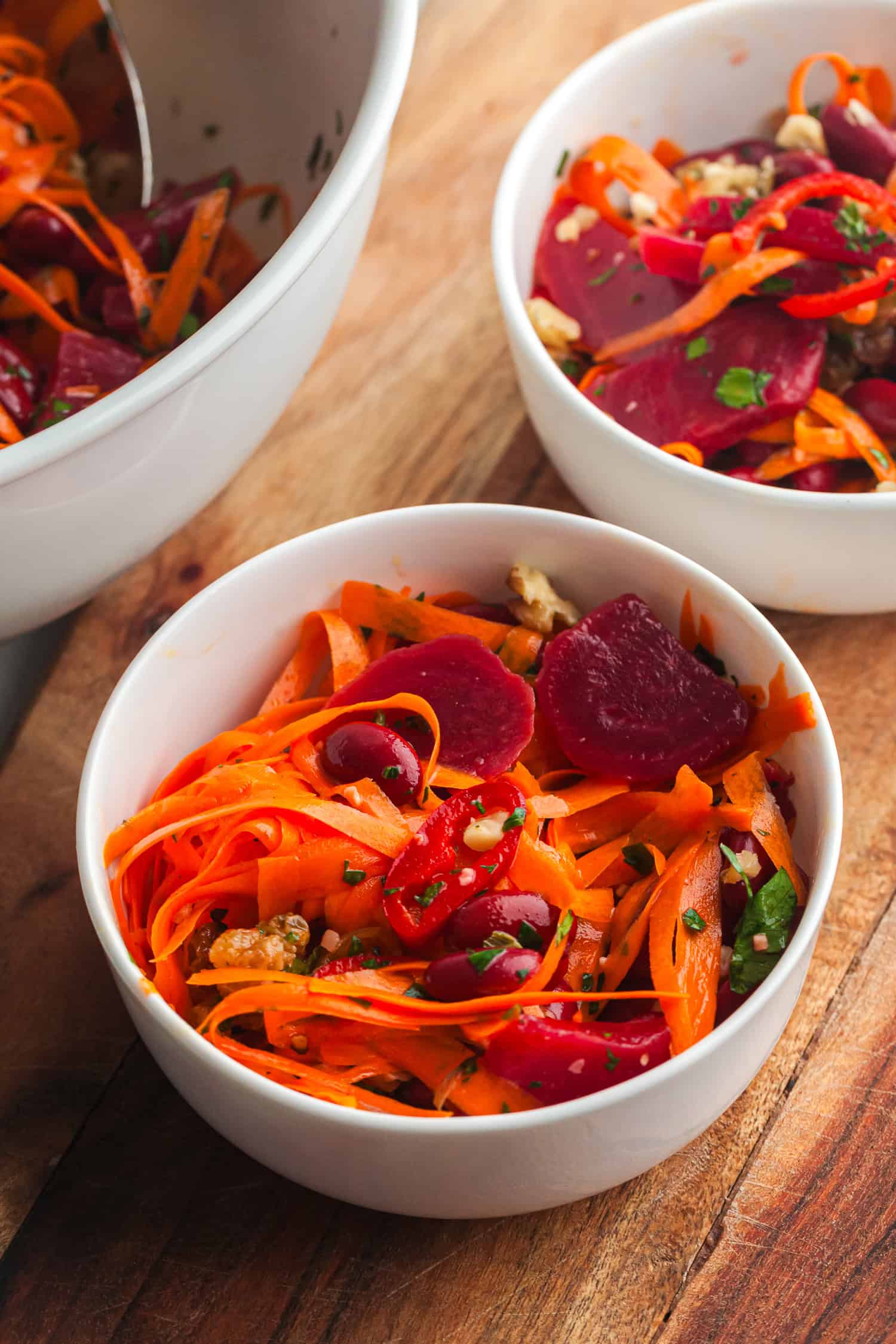 Carrot beet salad with sliced carrots, beets, walnuts, and parsley in white bowls on wooden table – healthy and colorful vegan dish