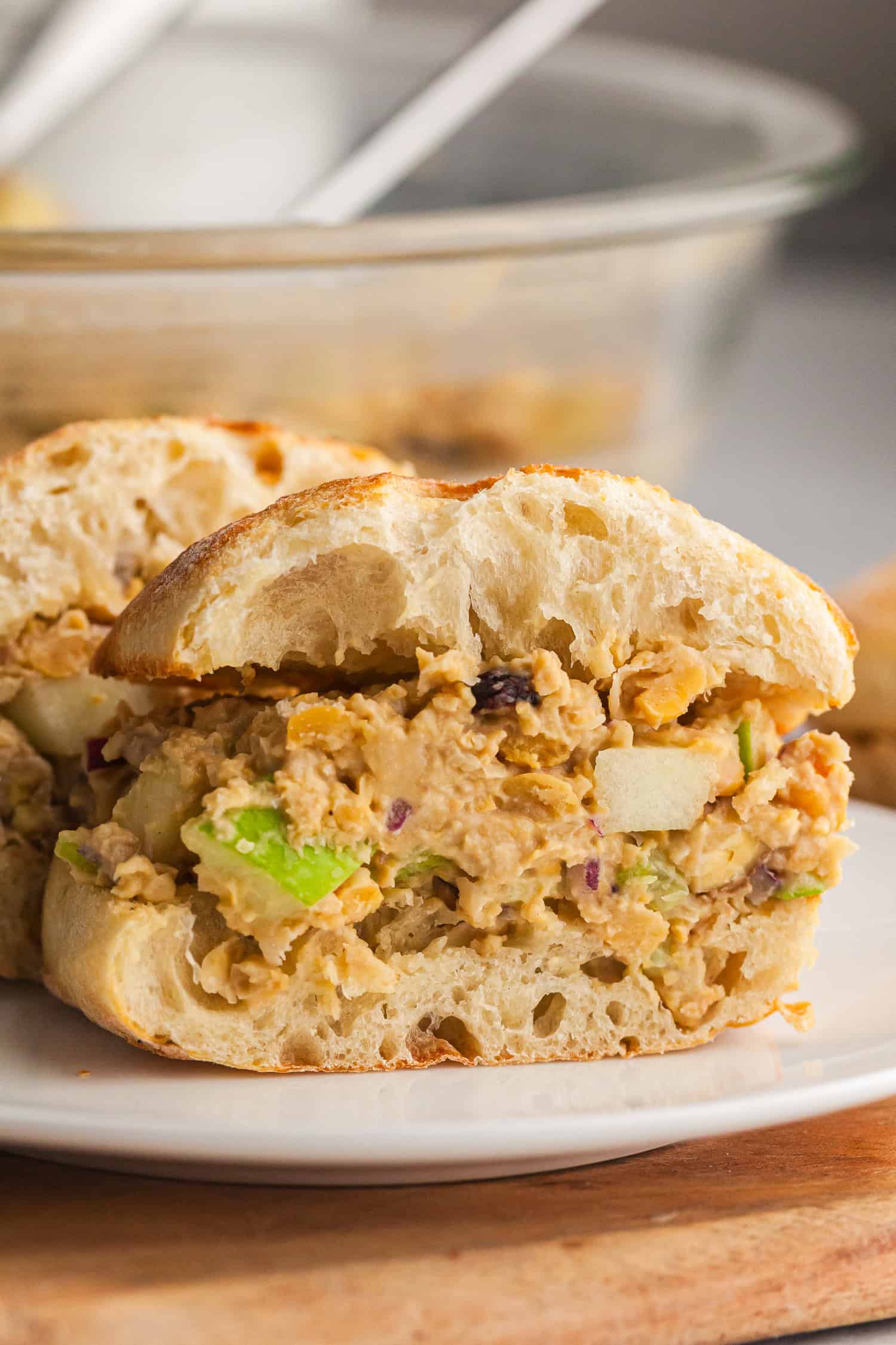 Crusty sandwich with chickpea chicken salad—apples, onion, and creamy filling on white plate.