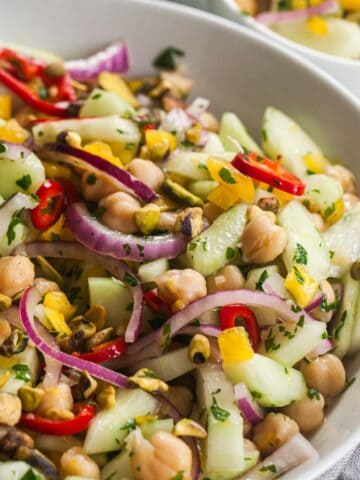 Cucumber and chickpea salad in a white bowl with onion, bell pepper, chili, parsley, and pistachios.