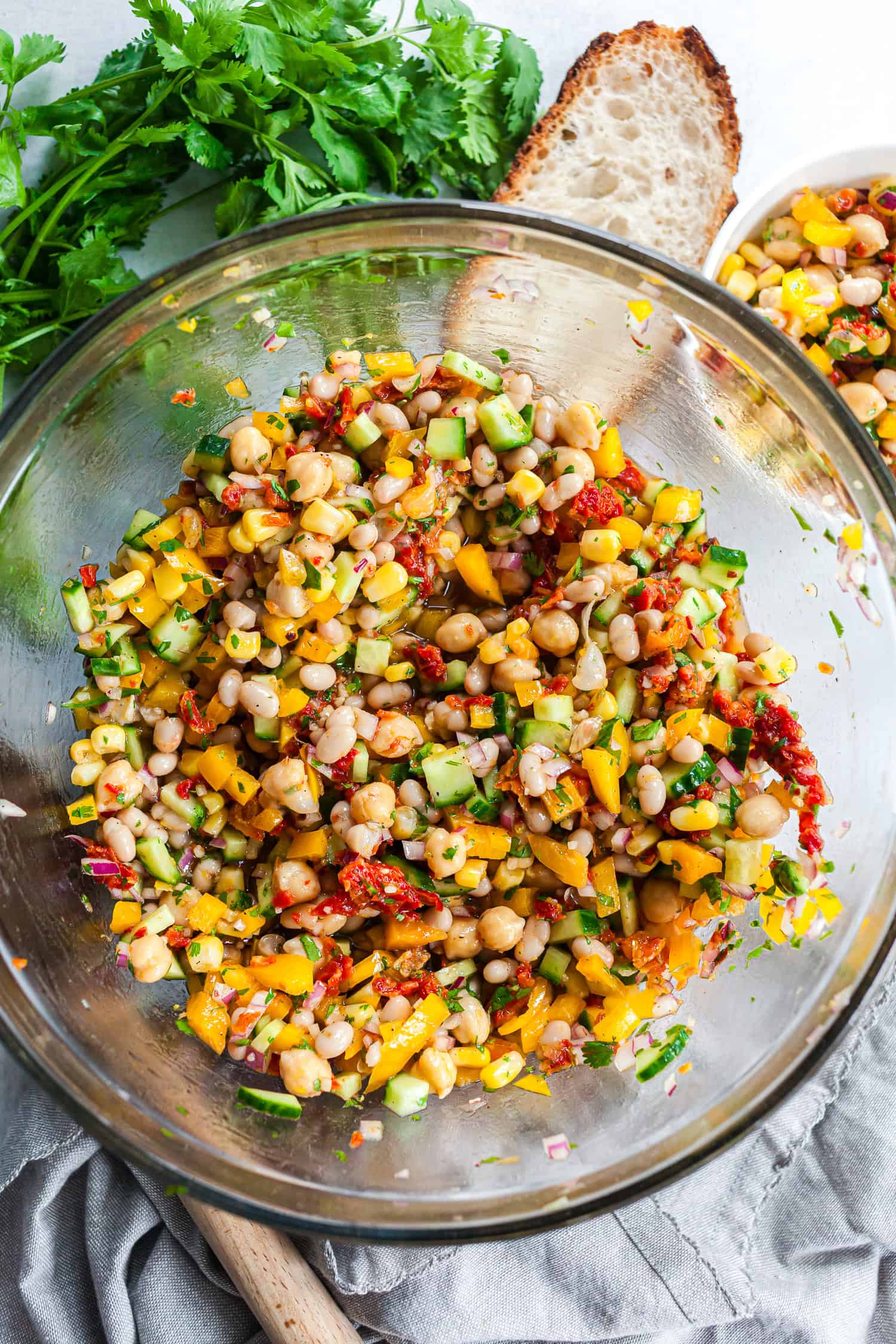 Large glass bowl of freshly mixed Dense Bean Salad with white beans, chickpeas, vegetables, and sun-dried tomatoes, ready to serve.