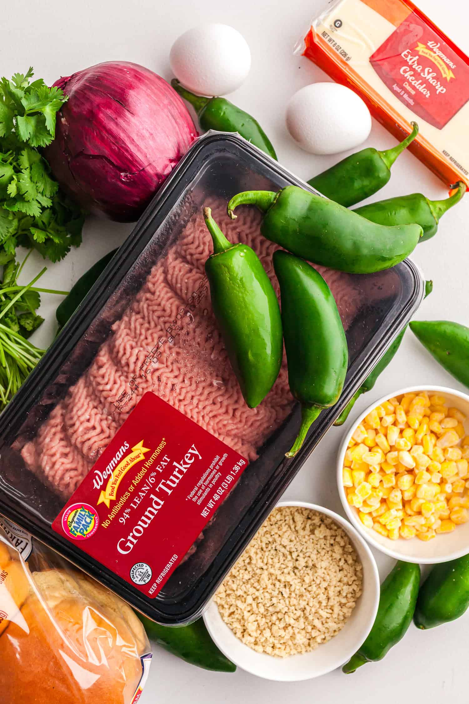 Fresh ingredients for homemade jalapeño turkey burger with cheddar—ground turkey, jalapeños, red onion, cilantro, eggs, cheddar cheese, corn, breadcrumbs, and burger buns.