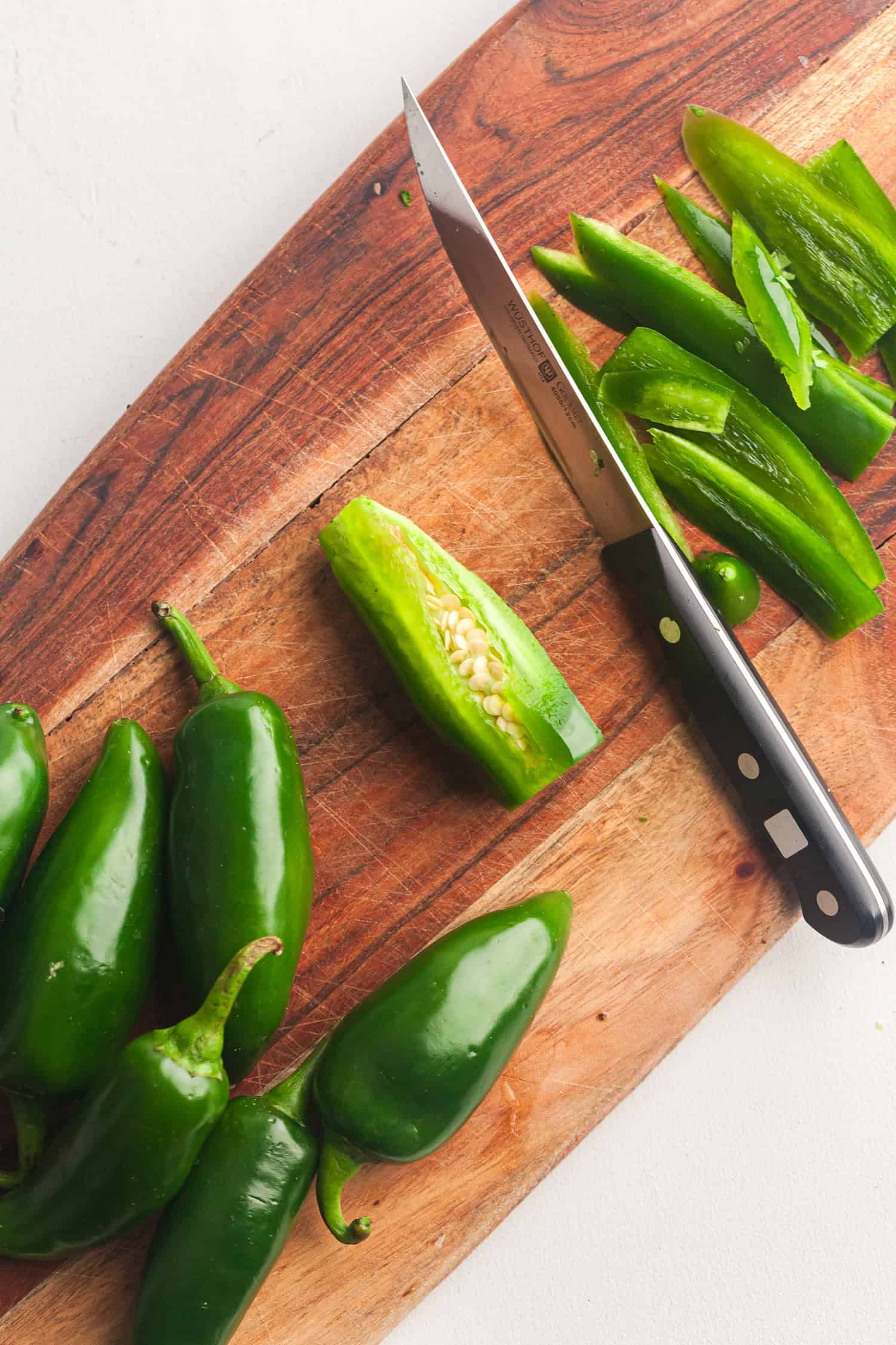 Fresh jalapeño peppers being sliced on a cutting board with a knife, ready for turkey cheddar burgers.