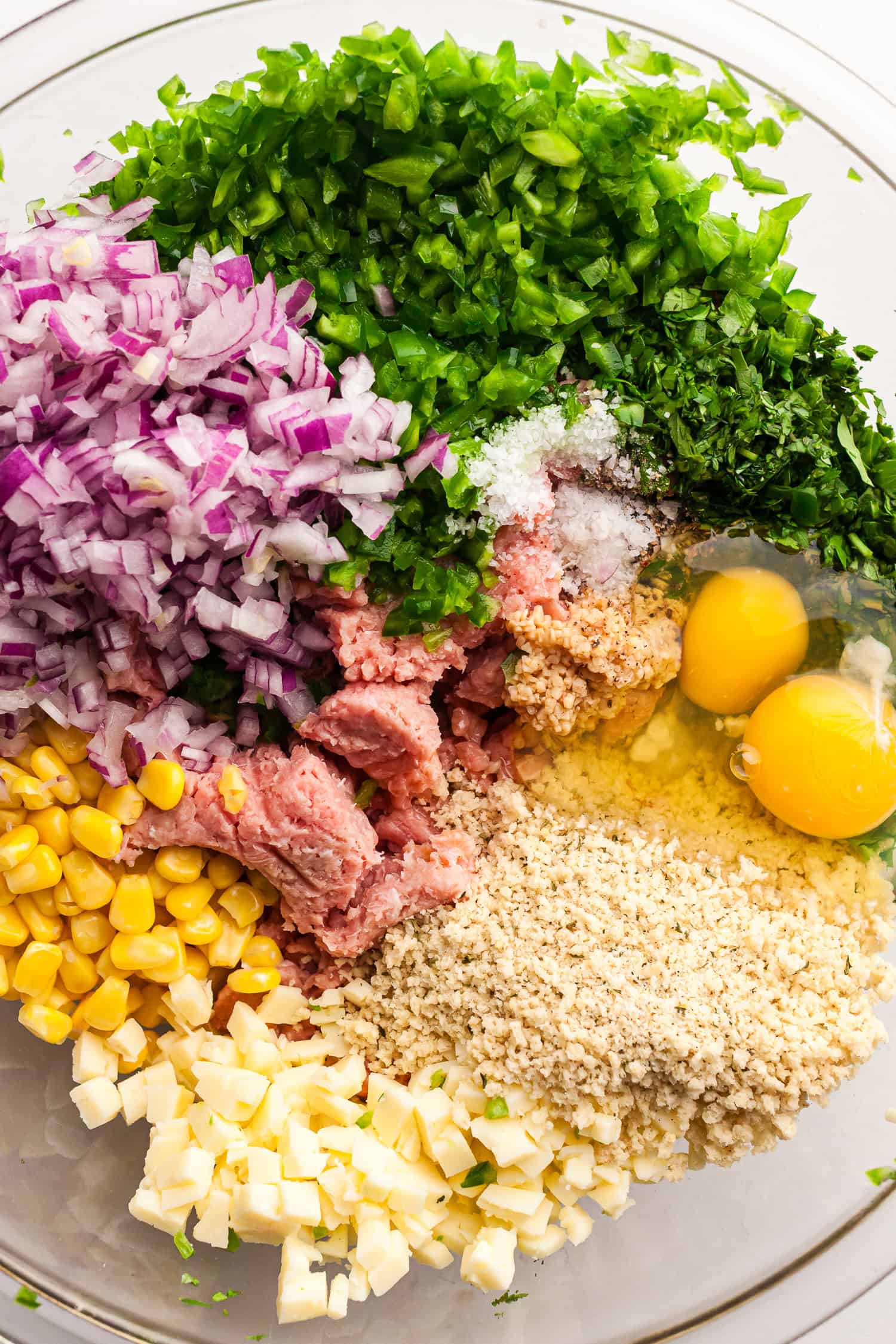 Bowl of ground turkey, chopped jalapeños, red onion, corn, cheese cubes, eggs, herbs, breadcrumbs, and seasonings for making jalapeño cheddar burgers.