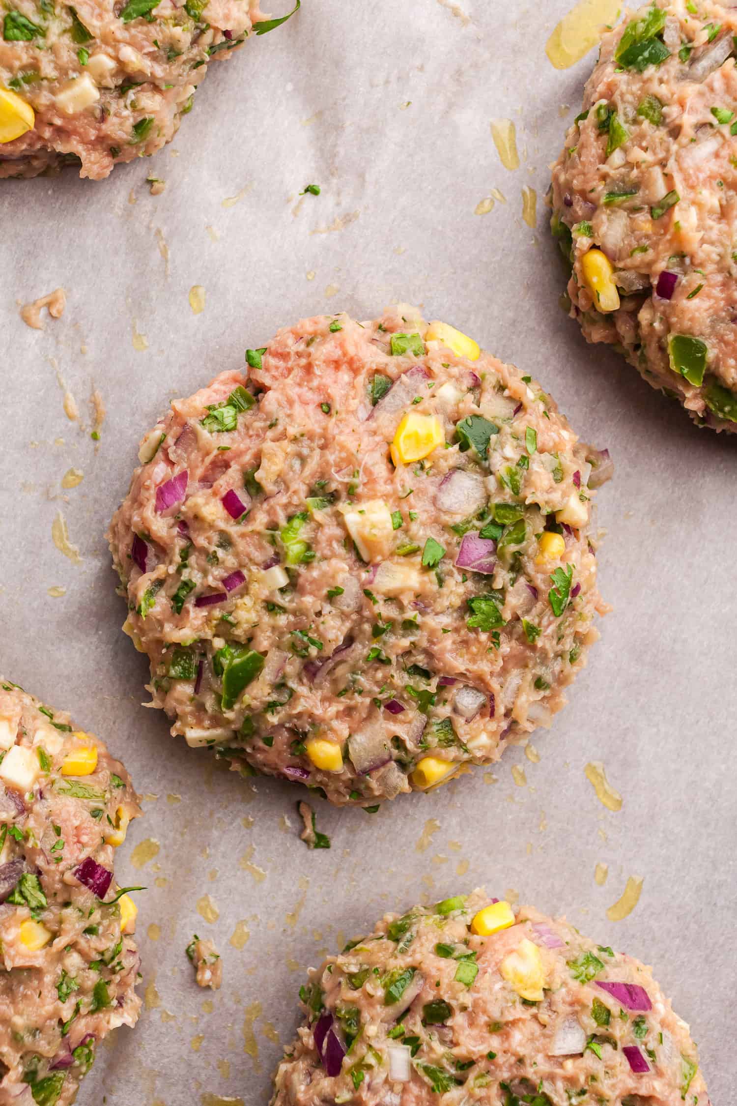 Uncooked jalapeño turkey burger patties with red onion, corn, herbs, and ground meat on parchment paper.