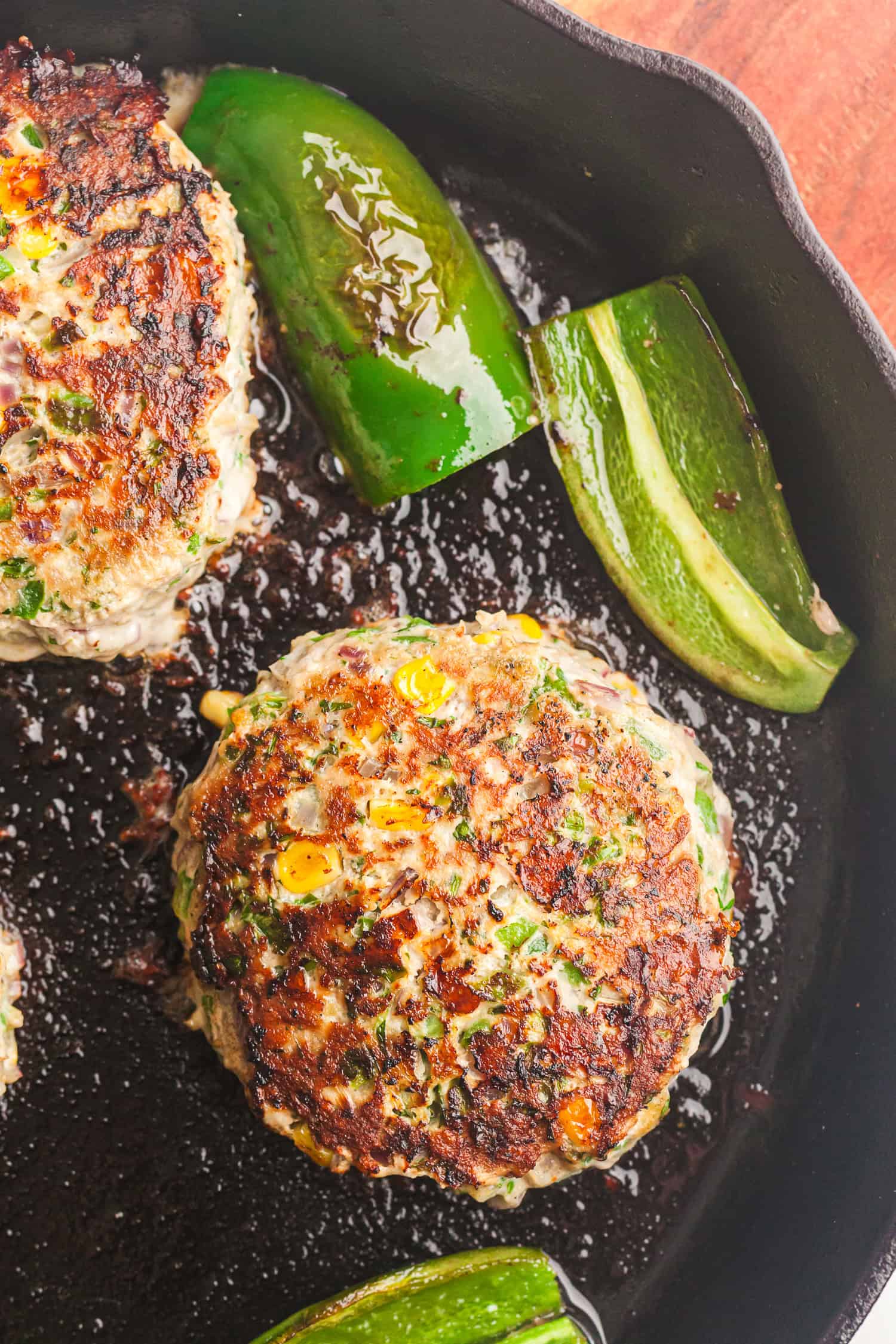 Turkey cheddar burger patties with corn and herbs cooking in a skillet with green bell peppers.
