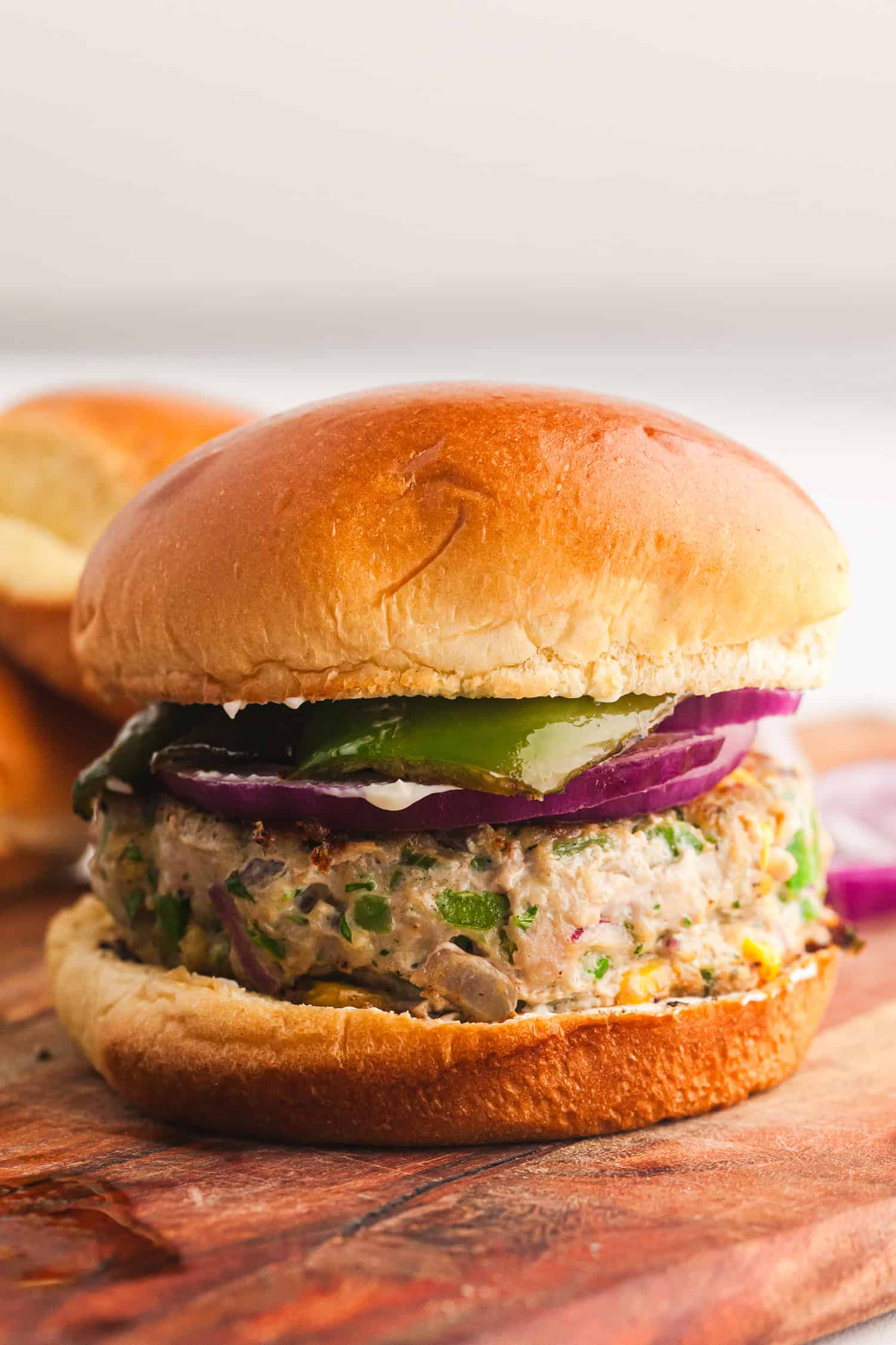 Turkey burger with cheddar, red onion, pickle, and creamy sauce on a toasted bun, served on a wooden surface.