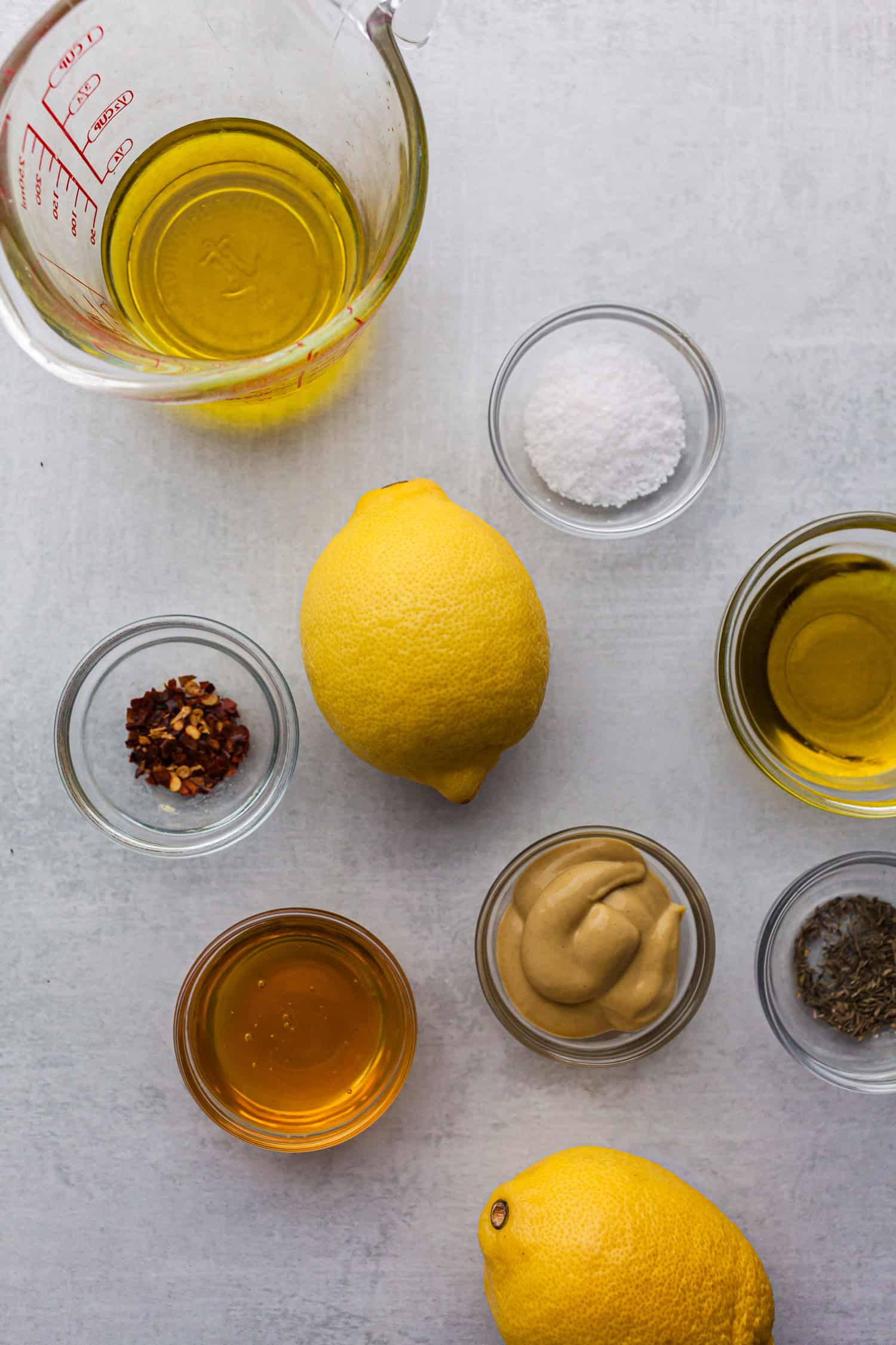 Ingredients for lemon dressing with olive oil, mustard, honey, herbs, and fresh lemons.