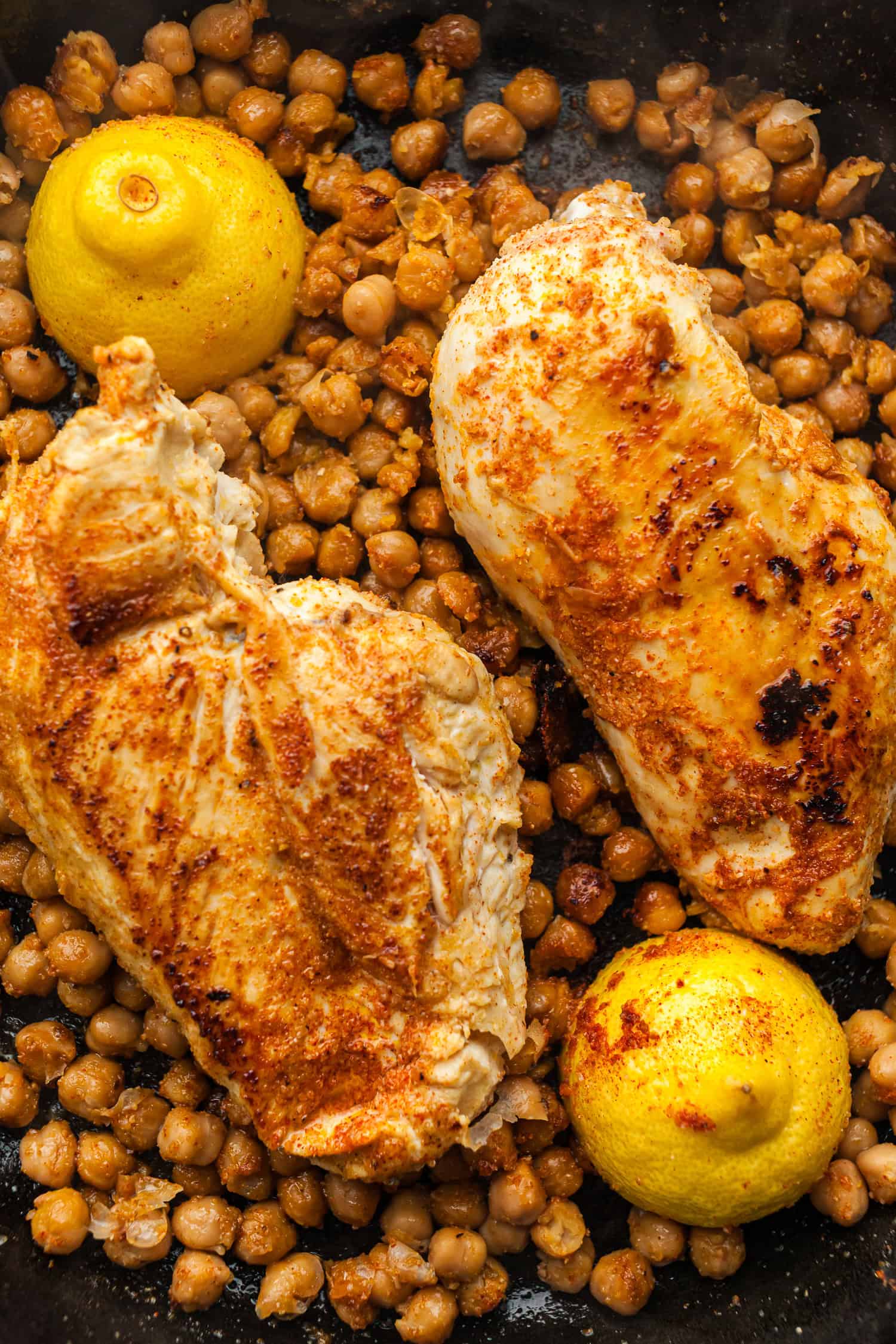 Grilled chicken with roasted chickpeas and whole cooked lemons on a plate.