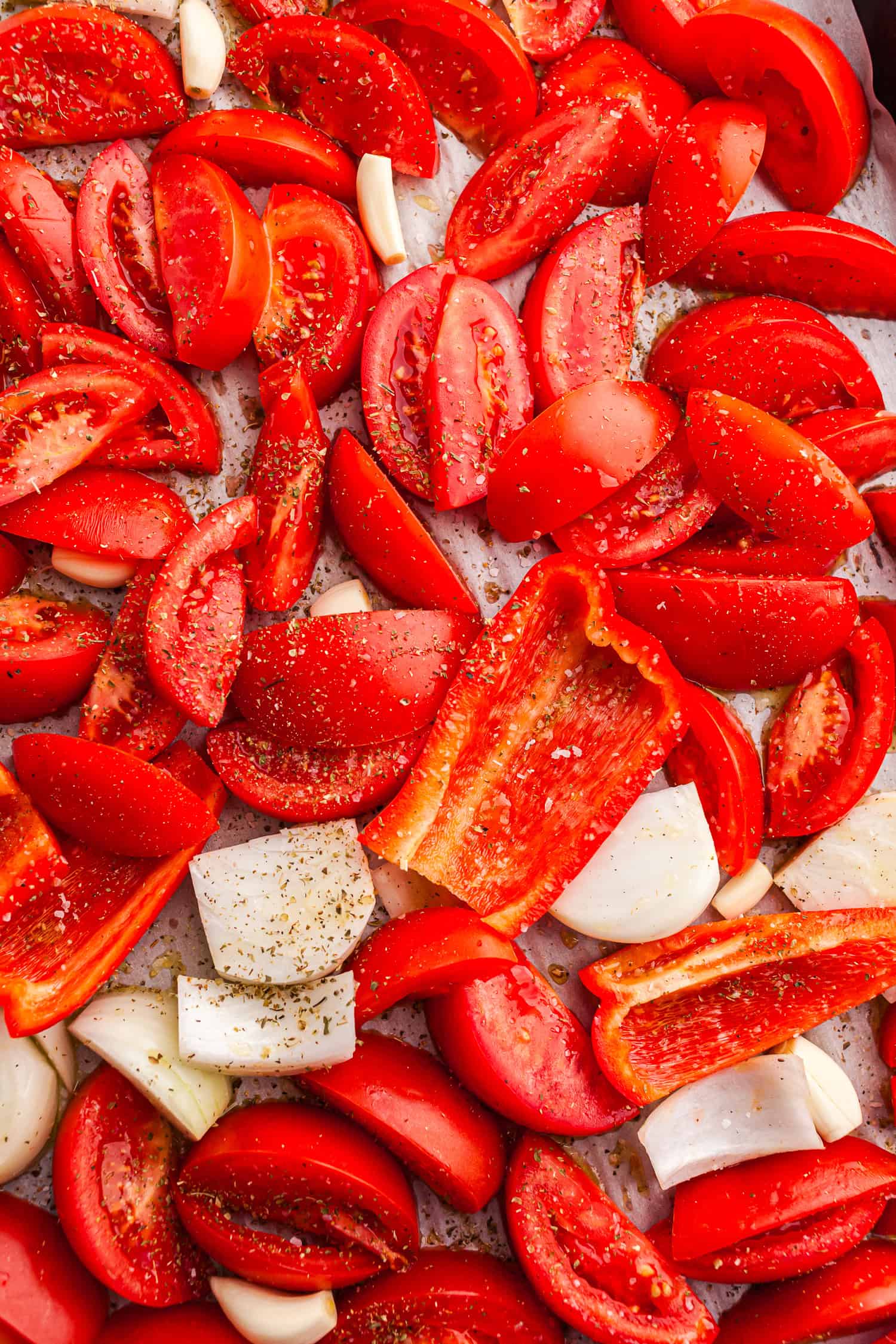 Tray of chopped tomatoes, peppers, onions, and garlic with herbs, ready for roasting.