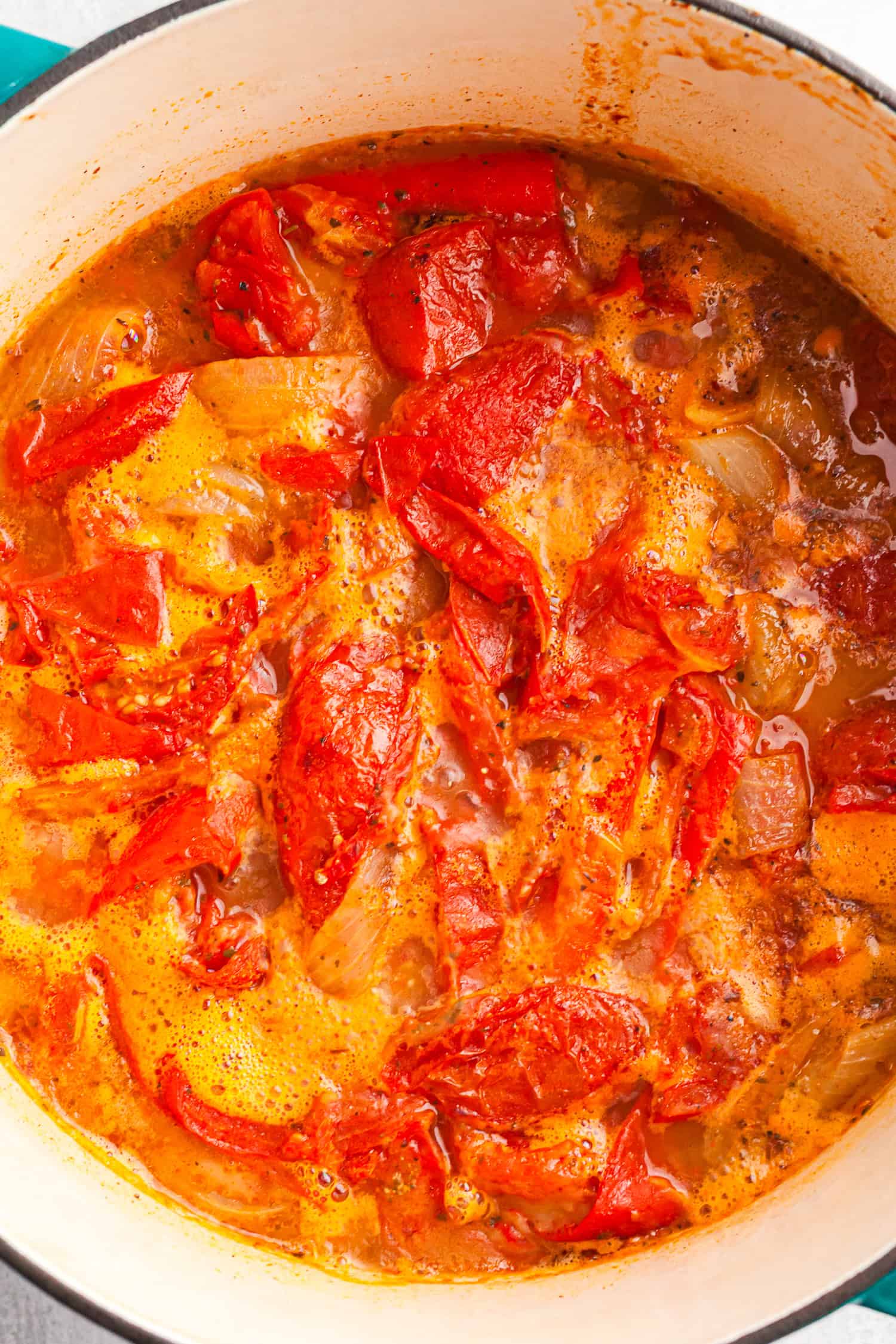 Cooked tomatoes and onions simmering in a rich, red broth inside a pot.