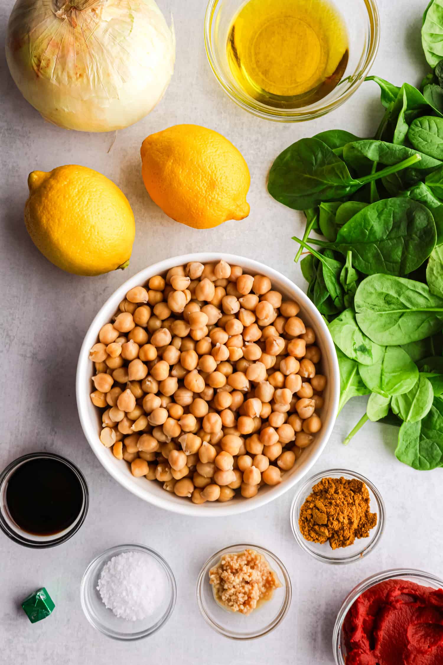 Fresh ingredients for chickpea stew including canned chickpeas, spinach, lemons, onion, and spices.