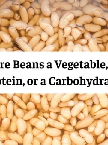 A close-up, overhead view of white cannellini beans soaking in water within a wooden bowl.