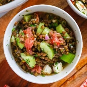 Top-down view of a white ceramic bowl filled with lentil and feta salad featuring pink grapefruit segments, cucumber slices, and fresh dill.