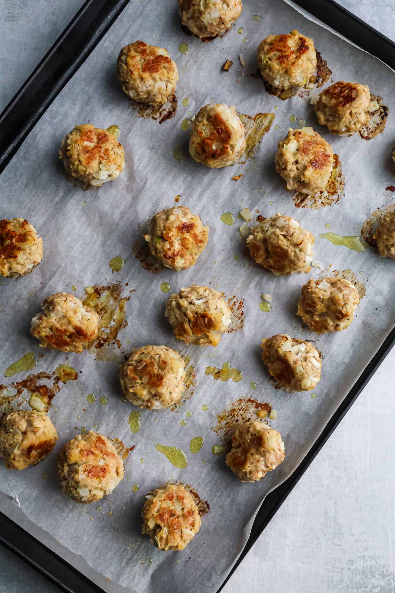 A top-down view of golden-brown chicken meatballs spaced evenly on a parchment-lined baking sheet after being removed from the oven.