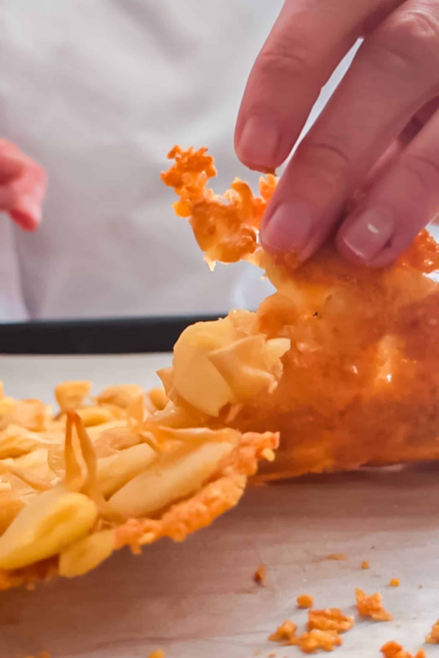A hand lifting a large, golden-brown shard of crispy baked parmesan and butter beans from a baking sheet.