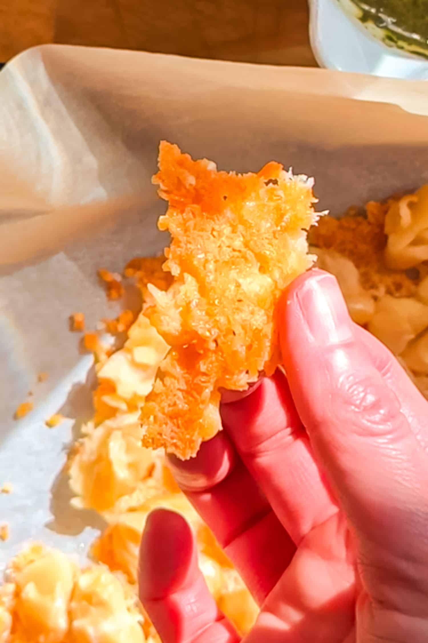 hand holds up a piece of golden-brown, crispy parmesan and butter bean crust over a parchment-lined baking sheet.