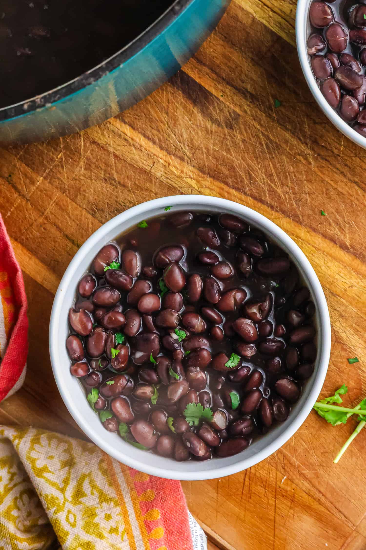 A top-down view of a small white bowl filled with cooked black beans and fresh cilantro on a wooden surface.