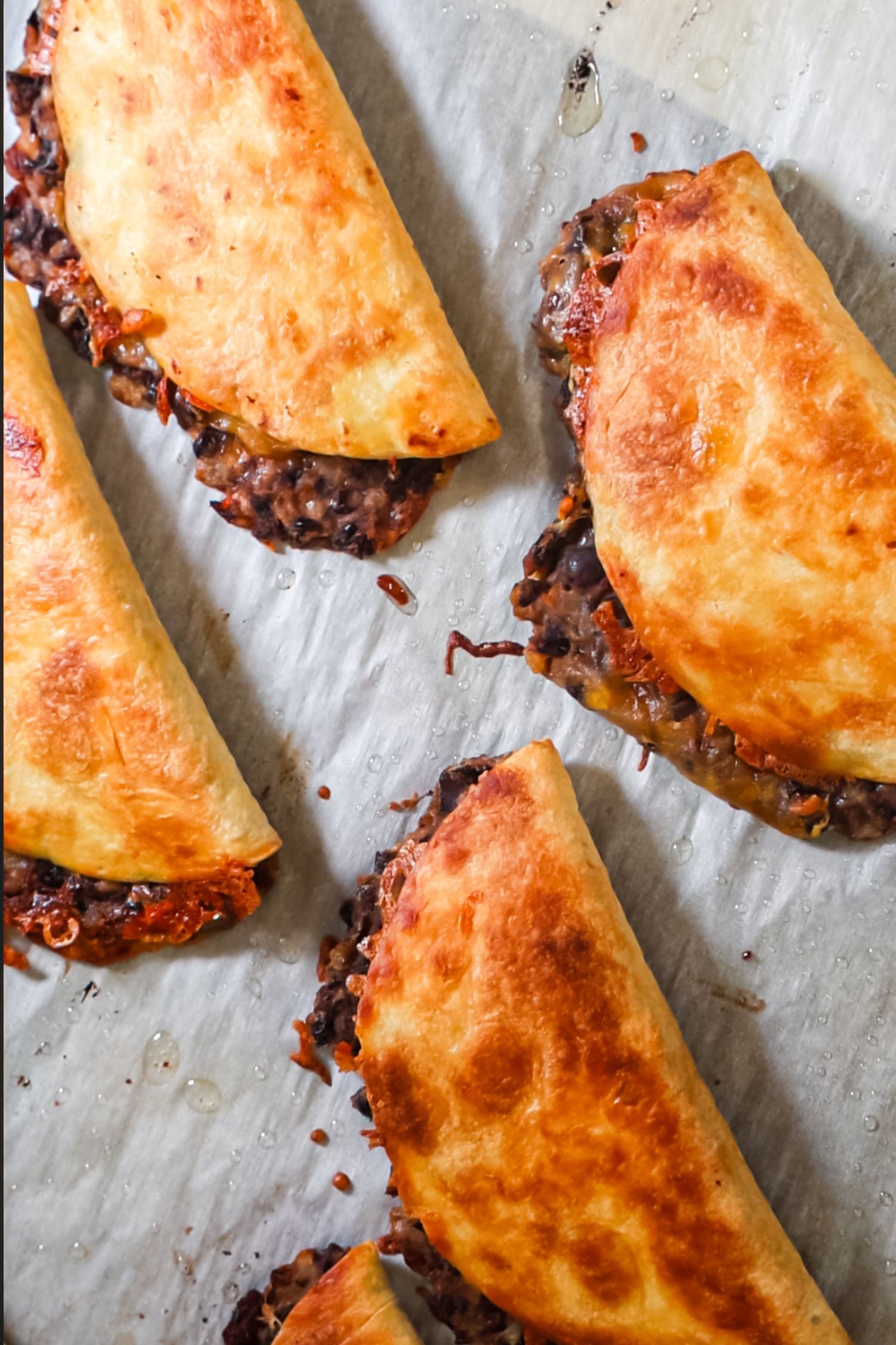 Four crispy, golden-brown baked tacos filled with black beans and melted cheese sit on white parchment paper.